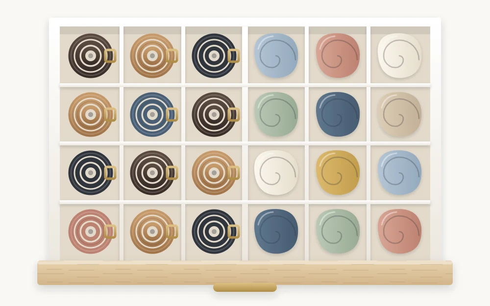 Top view of a shallow drawer divided into square compartments holding rolled belts and rolled scarves in soft colors